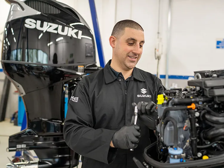 Ferry Marine - Suzuki outboard motor servicing and repairs A Suzuki-trained technician working on an outboard powerhead at the bench, a DF350 cowling behind